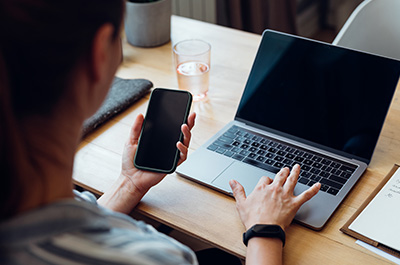 woman looking at phone and typing on computer