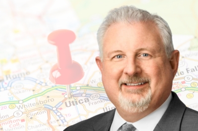 Tony Vitagliano, regional president of Excellus BlueCross BlueShield’s Utica Market, positioned in front of a map of New York State with a thumbtack marking Utica.